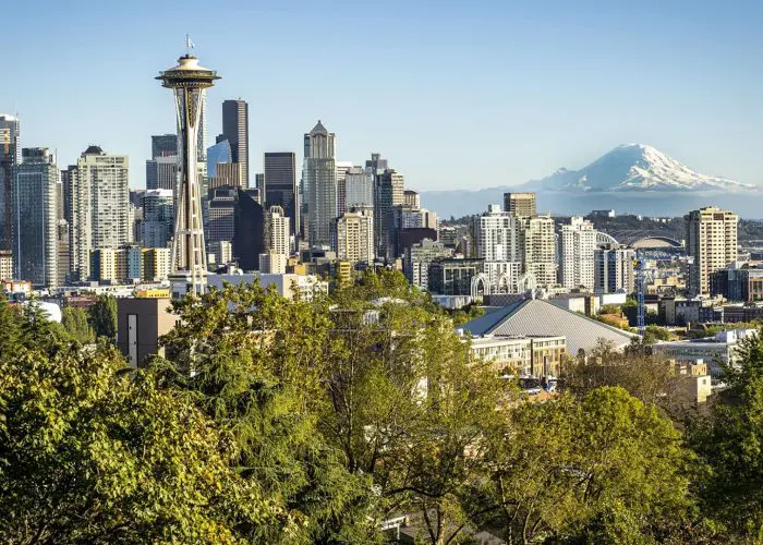 Seattle city skyline with the Space Needle in the foreground, skyscrapers in the center, and Mount Rainier in the background under a clear sky—a perfect view for tours utilizing Step-on Services.
